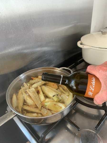 Adding a glass of wine to a frying pan of cooking fennel